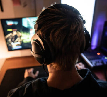 Rear View of Gamer with Headset on Playing Online Video Games in Dark Room
