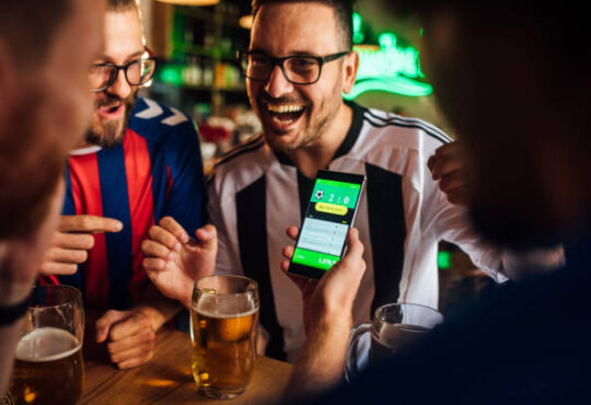 Soccer fans drinking beer at the pub and using mobile app for betting.
